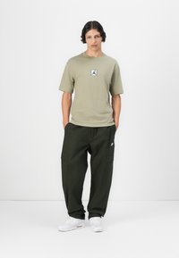 Oliven grøn t-shirt med logo, afslappet pasform; mørkegrøn cargo-bukser med sidelommer; hvide sneakers med en tekstureret overflade.