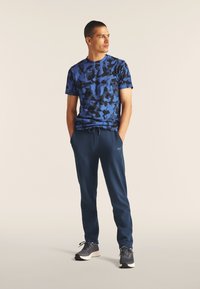 Camiseta de estampado de camuflaje azul con mangas cortas, combinada con pantalones jogger navy. El conjunto se completa con zapatillas deportivas grises.