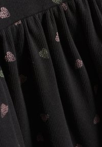 Svart tyg med ribbad textur har spridda små hjärtan i rosa och grönt. Mönstret är samlat för en flödande effekt.