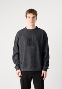 Svart stripet hettegenser med rund hals og senkede skuldre. Har en subtil "HUGO" logo trykket på forsiden. Laget av strukturert stoff.