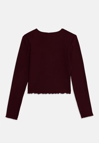 Burgundy long-sleeve ribbed top with a cropped cut and wavy hem. Features a round neckline and fitted sleeves. No visible fasteners.