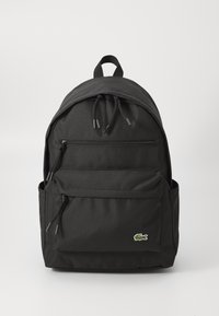 Sac à dos noir en nylon avec un dessus arrondi, deux poches zippées à l'avant et des poches latérales. Comprend des fermetures à cordon et un petit logo à l'avant.