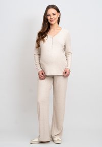 Beige långärmad topp med henley-krage, tillsammans med matchande vida byxor, båda gjorda av mjuk, strukturerad tyg.