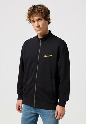 Chaqueta negra con cremallera hecha de tela suave, con cuello alto y el logo de "Wrangler" bordado en dorado en el lado izquierdo del pecho.