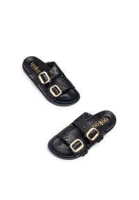 Chanclas negras con dos correas en forma de concha y hebillas doradas. Elaboradas con un material texturizado, cuentan con una plantilla suave y un detalle del logo.