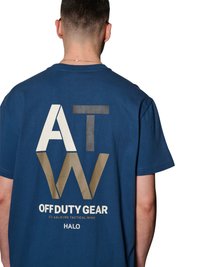 Mand iført blå T-shirt med store hvide, sorte og guld bogstaver "ATW" og teksten "OFF DUTY GEAR 223 AALBORG TACTICAL WING HALO" på ryggen.