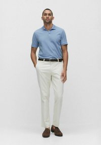 Ljusblå pikétröja med korta ärmar, vita byxor, mörkt flätat bälte och bruna loafers. Enkelt mönster och neutral färgskala.