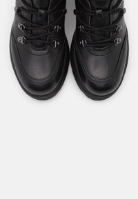 Bottes de randonnée noires en cuir avec bouts arrondis, crochets métalliques pour les lacets et surfaces texturées, présentant des détails de coutures proéminentes.