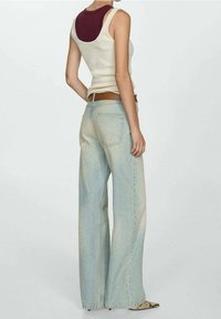 Beige ilmanhihaisessa topissa kerroksittain maroon tankin päällä, yhdistettynä vaaleansinisiin leveälahkeisiin farkkuihin. Vöinä on ruskea vyö ja kengät ovat kuvioidut.