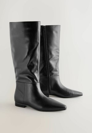 Ein Paar schwarze kniehohe Lederstiefel mit spitzen Zehen und seitlichen Reißverschlüssen auf einem hellen Hintergrund.