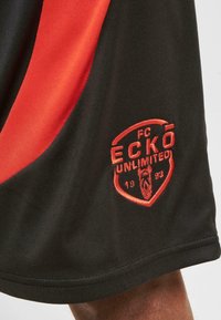 Black athletic shorts with red accents. Features an embroidered logo in red and black, with smooth fabric and a relaxed fit.