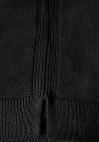 Tissu en tricot noir avec un motif texturé et côtelé. Présente une couture proéminente et un petit trou au centre en bas. Texture douce.