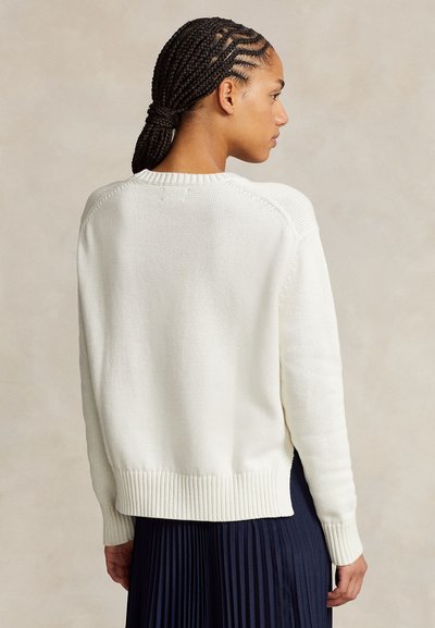 Kreminės spalvos megztinis su tekstūruotu raštu, ribuotais rankogaliais ir apačia. Nugaroje – apvalus kaklas ir laisvas siluetas.