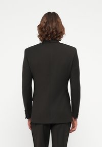 Svart skreddersydd blazer med krage, enkel splitt bak og knappede mansjetter. Glatt tekstur, tettsittende fasong.