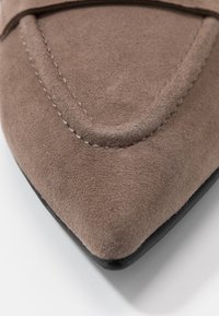 Semišové boty s špičatou špičkou v světle hnědé barvě s texturovaným povrchem a kontrastní černou podrážkou. Viditelné švy podtrhují design.