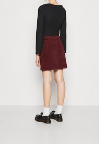 Falda mini de pana burdeos con corte recto y bolsillos traseros, combinada con zapatos de plataforma negros y calcetines blancos. Top de manga larga negro.