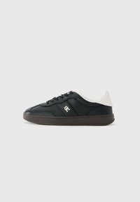 Zwarte lage sneakers met een witte gepluche kraag, zwarte veters, een bruine zool en een klein metalen logo op het zijpaneel.