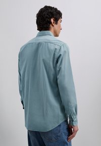 Lichtblauw overhemd met lange mouwen van zachte stof, voorzien van een puntkraag, knoopmanchet en een detail op het rugpand. Met een afgeronde zoom en een comfortabele pasvorm.