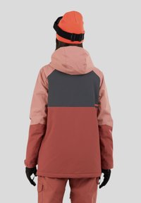 Kurtka na zewnątrz w różowym, szarym i rdzawego kolorach; ma kaptur, regulowany krój i teksturowany materiał; zestawiona z pomarańczową czapką.