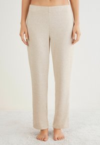 Beige wijde broek van zacht, rekbaar materiaal met een subtiele textuur en een soepel elastische tailleband. Zoom tot op de vloer, geen zichtbare zakken.