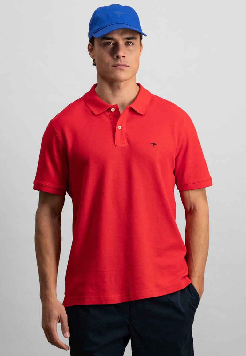 Rød polo skjorte med klassisk krage og korte ermer, med en liten marineblå logo. Sammen med en blå caps, vist mot en nøytral bakgrunn.