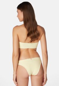 Gul texturerad bikiniuppsättning med bandeau-top och lågmidjade bottnar, med en liten knappdetalj på baksidan av bottnarna.