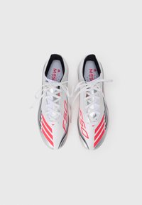 Balti, sidabriniai ir raudoni Adidas futbolo batai su surištais raišteliais, matomi iš viršaus ant paprasto balto fono.