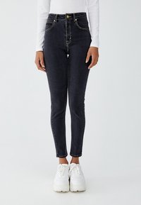 Černé džíny s vysokým pasem, slim fit, s kontrastními žlutými švy, předními kapsami a zipem, doplněné bílými teniskami.