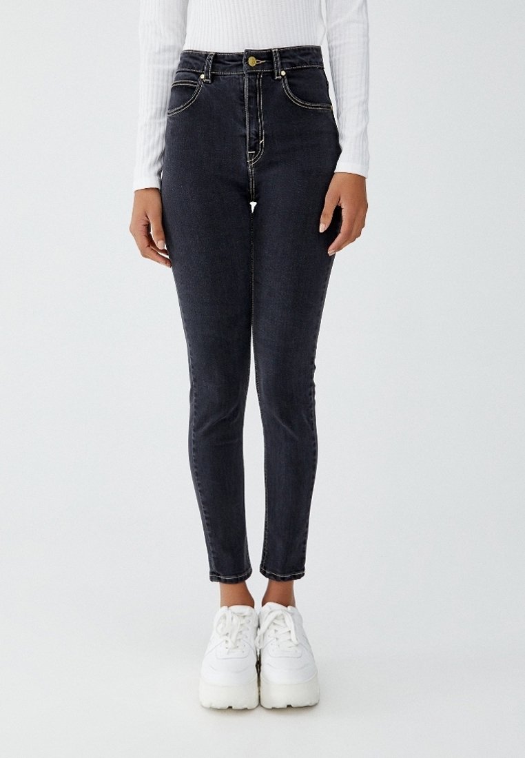 Černé džíny s vysokým pasem, slim fit, s kontrastními žlutými švy, předními kapsami a zipem, doplněné bílými teniskami.