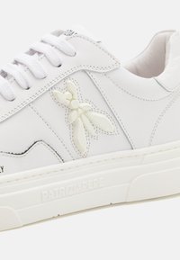 Baskets en cuir blanc avec des accents texturés, présentant un élément décoratif en relief sur le côté, des lacets ronds et une semelle en caoutchouc blanc.