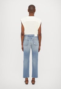 Haut en maille blanche avec manches courtes, associé à un jean bleu clair droit avec des ourlets effilochés et un léger délavage, porté avec des sandales marron.