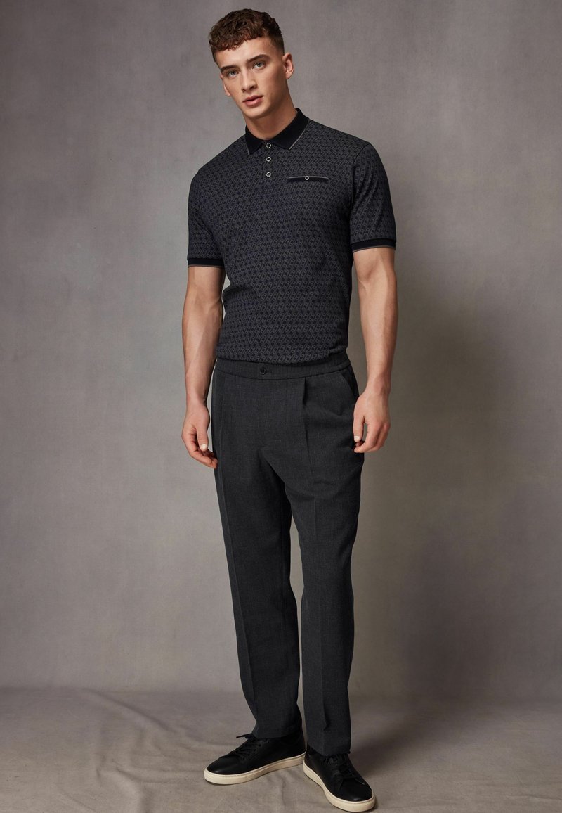 Tee-shirt polo cu model naval, cu guler, asortat cu pantaloni gri tip tailored și adidași negri. Ținuta prezintă accente și texturi subtile.