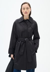 Svart trenchcoat med krage, bälte i midjan, stora framfickor och knappstängning. Slätt tyg och långa ärmar.