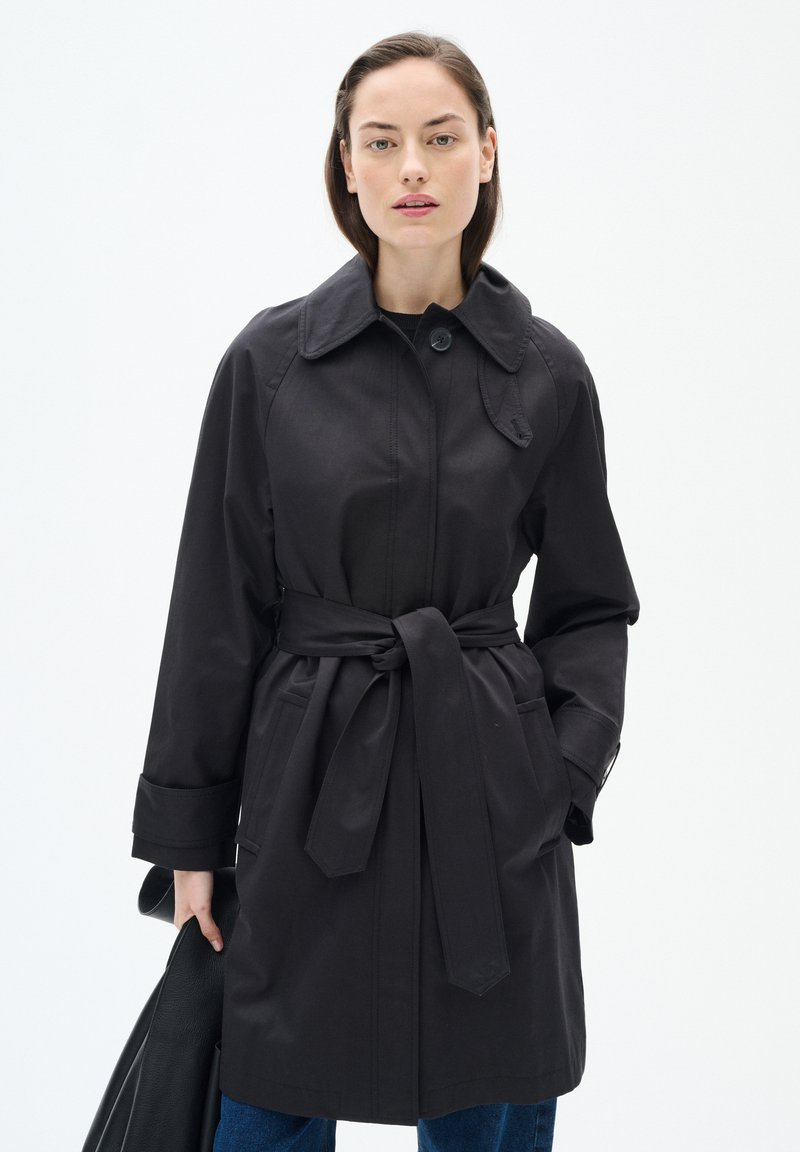 Svart trenchcoat med krage, bälte i midjan, stora framfickor och knappstängning. Slätt tyg och långa ärmar.