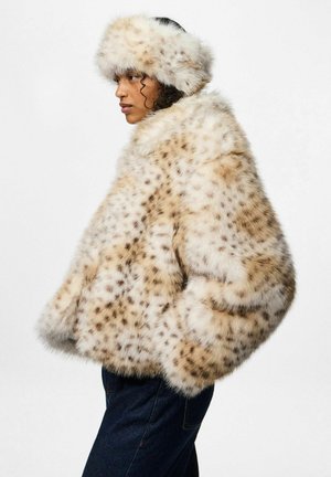Cappotto in pelliccia sintetica con una base beige chiaro, macchie scure e un colletto morbido. Abbinato a un cappello di pelliccia coordinato. Jeans di denim scuro visibili.
