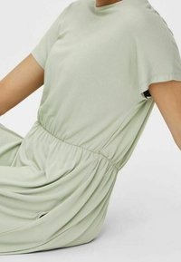 Svěže zelené šaty s krátkým rukávem a elastickým pasem. Jemná, splývavá látka s hladkou texturou. Neformální design vhodný pro různé příležitosti.