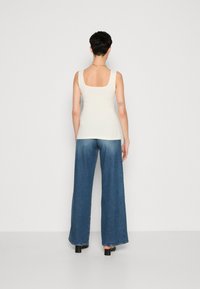 Débardeur beige clair avec un design de dos carré, associé à un jean en denim bleu à jambes larges et des chaussures à talons blocs noirs.