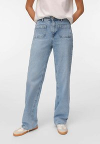 Pleekõrvale sinised denim teksad sirge jalaga disainiga, millel on kaks tagataskut ja kulunud äär. Kombineeritud beezide sneakersitega.