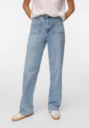Pleekõrvale sinised denim teksad sirge jalaga disainiga, millel on kaks tagataskut ja kulunud äär. Kombineeritud beezide sneakersitega.