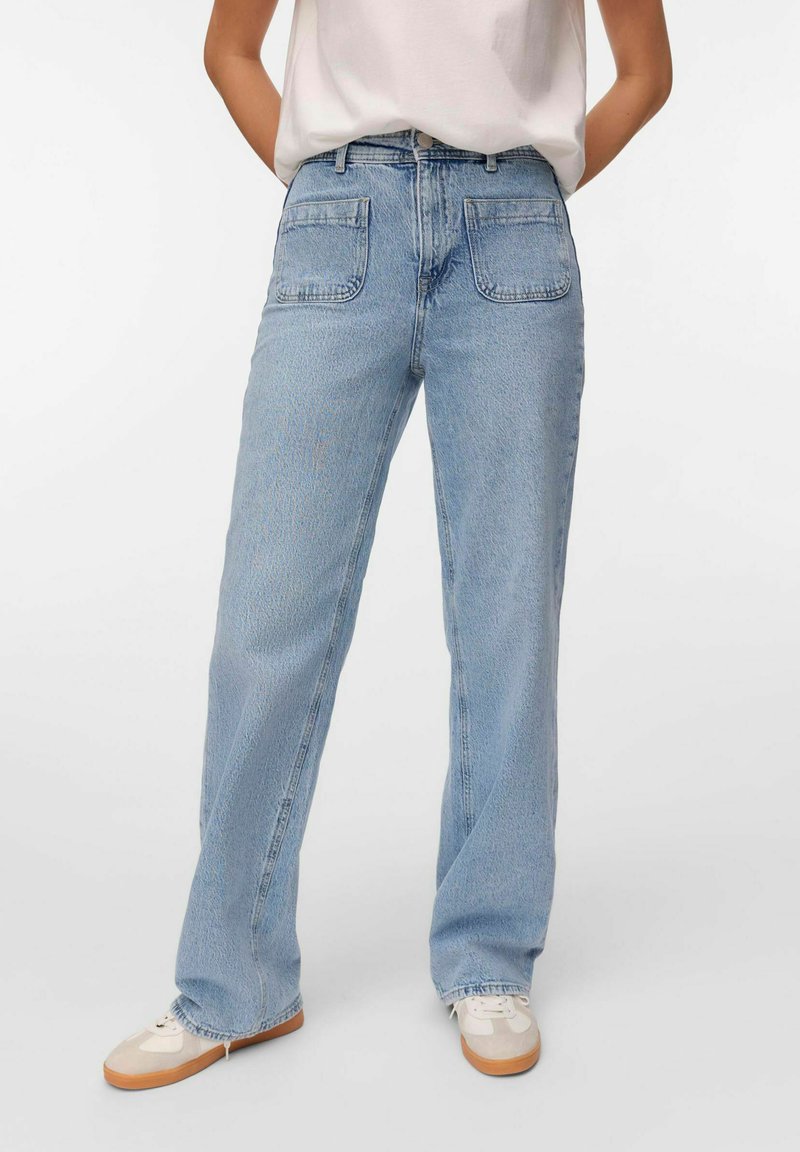 Pleekõrvale sinised denim teksad sirge jalaga disainiga, millel on kaks tagataskut ja kulunud äär. Kombineeritud beezide sneakersitega.