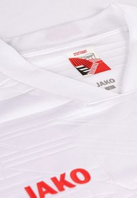 Maglia sportiva bianca con dettagli testurizzati, logo JAKO in rosso e un design di cucitura. L'etichetta riporta "Stuttgart" e la taglia "L".