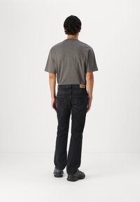 Camisa gris de manga corta combinada con jeans negros, con un corte recto y detalles en el bolsillo trasero. Los zapatos tienen un diseño grueso.