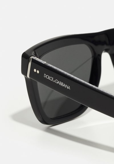Mustad mustad päikeseprillid tumepruunide läätsedega, mille käe kohal on hõbedane aktsent ja "DOLCE & GABBANA" bränding valges tekstis.