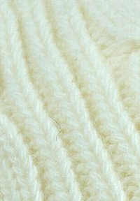 Tessuto lavorato a maglia di colore crema con un motivo testurizzato in rilievo. Fili morbidi e peluche creano un aspetto accogliente e caldo.