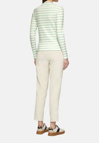 Un haut à manches longues rayé vert clair et blanc, associé à un pantalon en velours côtelé beige et des baskets blanches avec des accents noirs et dorés.