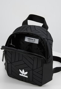 Svart ryggsäck med geometriskt mönster, utrustad med en framficka med dragkedja, justerbar rem och en vit adidas-logotyp på framsidan.