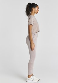 Vaaleanpunainen lyhyt t-paita, joka on yhdistetty yhdisteisiin istuviin leggareihin, joissa on teksturoitu kangas ja brändäys lahkeessa. Päällä valkoiset urheilu kengät.