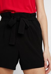Shorts noirs avec une large ceinture et un détail de nouage à l'avant. Fabriqués en tissu doux, dotés de deux poches latérales et d'une coupe décontractée.