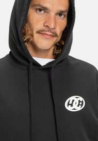 Black hoodie with a front kangaroo pocket, drawstring hood, and a white DC logo. Smooth fabric texture; relaxed fit.