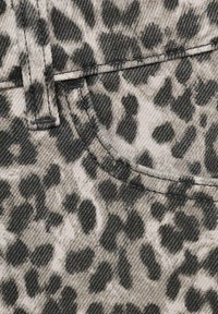 Tkanina s uzorkom leoparda koja se sastoji od sive i crne mrljaste šare, s vidljivim šavom i detaljima džepa na traper materijalu.